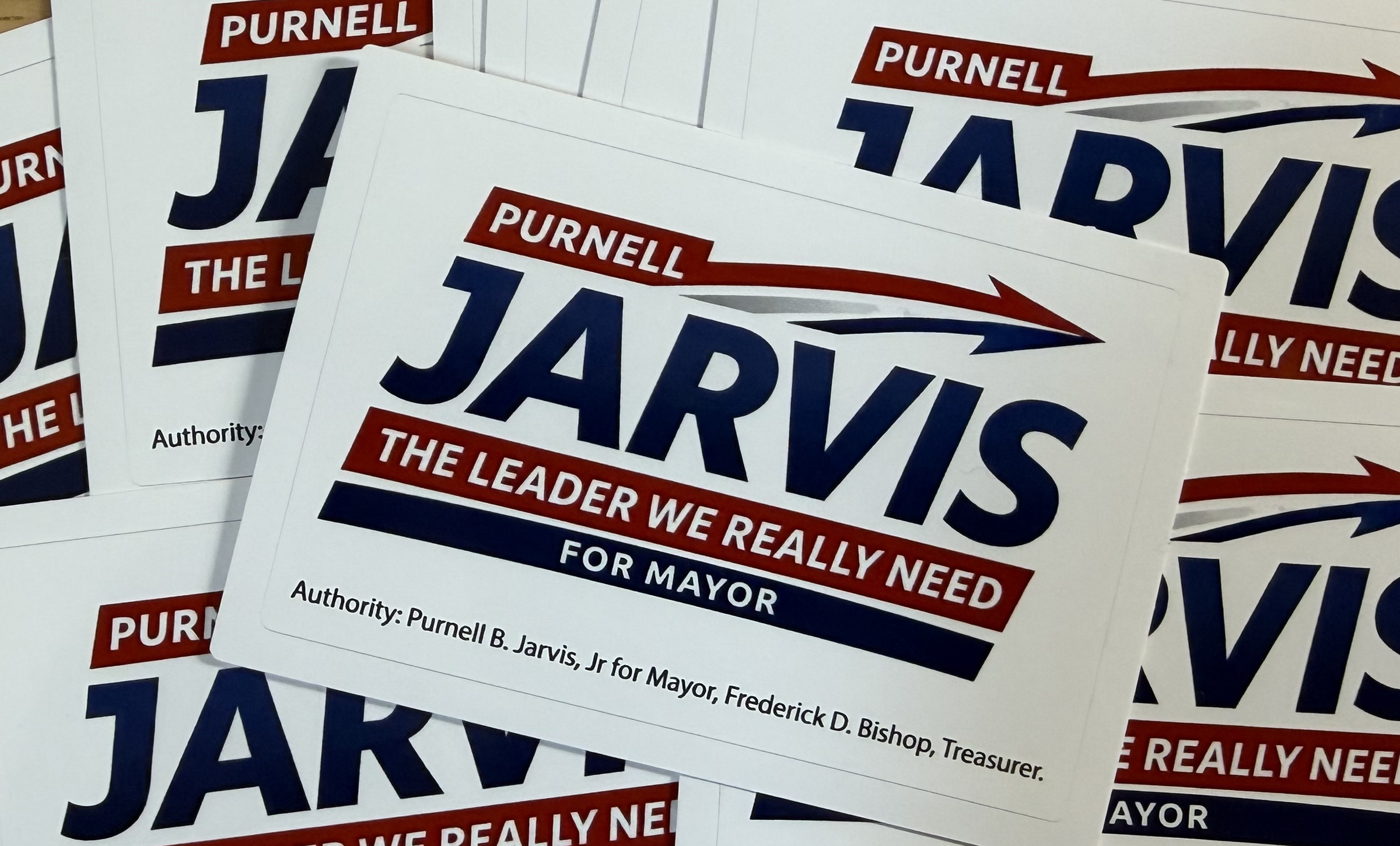 Small white Purnell Jarvis for Mayor stickers fanned out on a wooden surface
